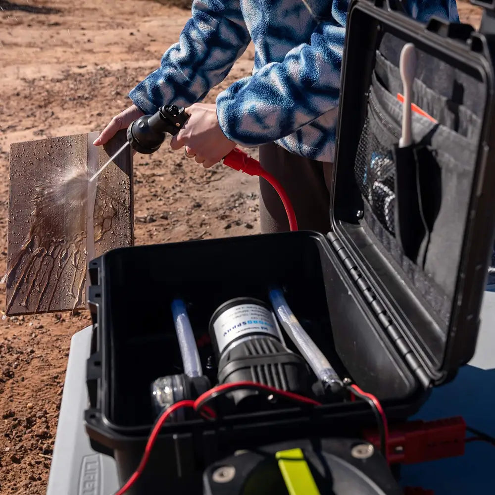 Person using a hose to spray down cutting board with an open HydroSpray container in the foreground.