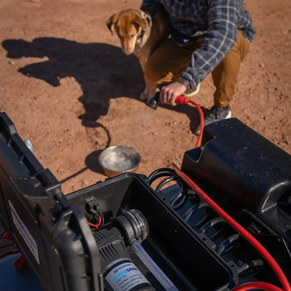 Person using the HydroSpray to fill up a water bowl with a dog standing nearby on a dirt surface.