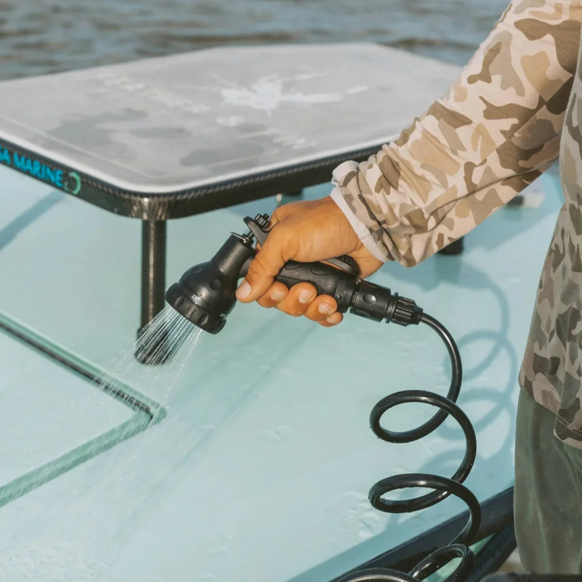 A hand holds a coiled-hose spray nozzle to rinse off the deck of a boat.