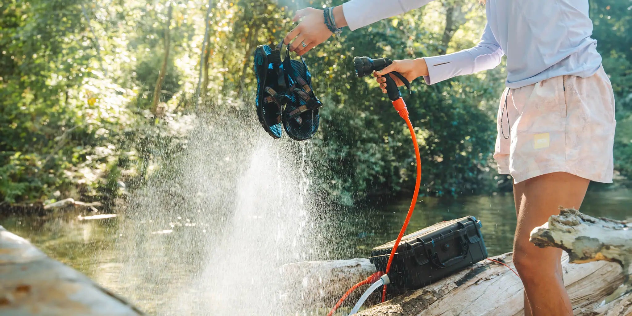 Person cleaning sandals with a water hose powered by an HydroSpray next to a river