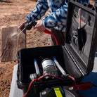 Person using a hose to spray down cutting board with an open HydroSpray container in the foreground.