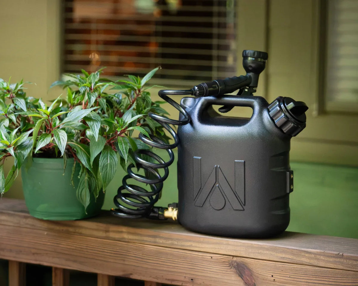 WaterPORT 2-gallon GoSpout on a porch railing next to a potted plant, with its coiled hose and nozzle in place.