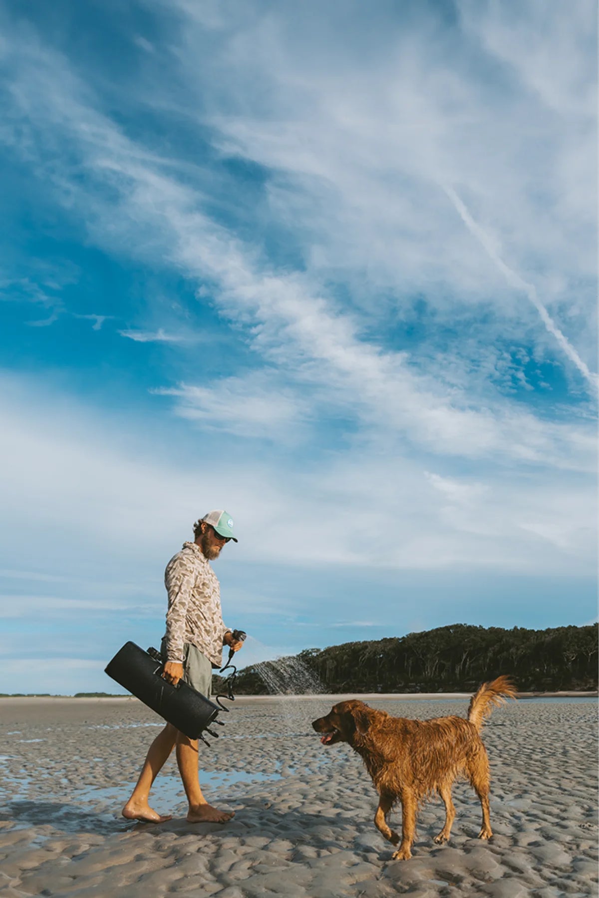 A man walks along a sandy beach with a dog, carrying a 4-gallon DayTank.